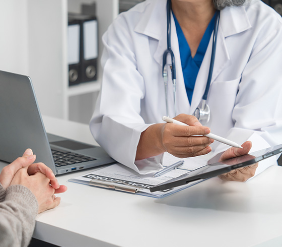 doctor consulting patient in modern office with laptop and medical chart discussing two health options and treatment plan