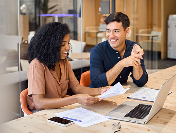 two colleagues collaborating in a modern office discussing project materials while seated at a table with a laptop and documents promoting teamwork and communication 3 tips for success