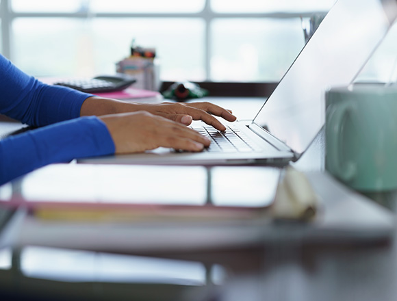 person typing on a laptop with hands positioned on the keyboard in a home office setting emphasizing productivity with five essential tools visible in the background
