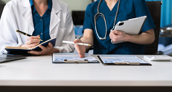 two medical professionals discussing patient information with charts and tablets on a table