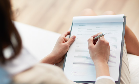 person filling out a form with a pen on a clipboard focusing on details and information for a particular purpose